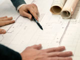 Två par händer granskar byggnadsritningar som ligger på ett bord