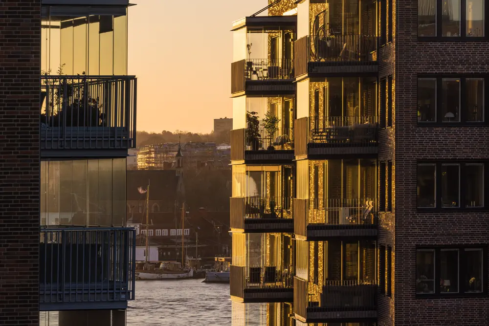 Lägenhetshus med glasbalkonger med vattnet i bakgrunden.