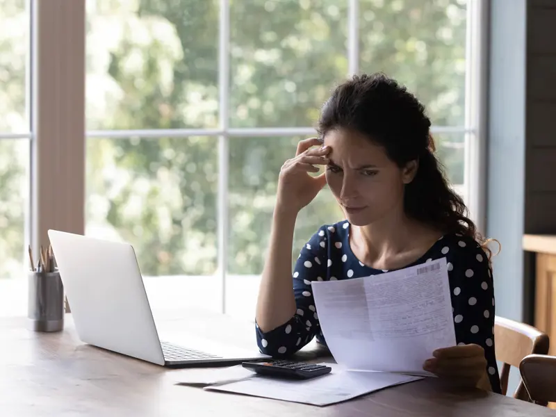 Kvinna funderar över en pappersfaktura vid sin laptop.