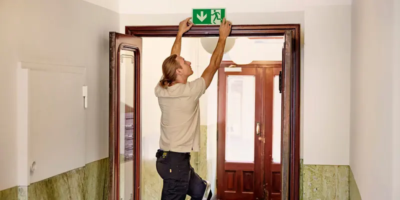 Man från Presto sätter upp skylt för nödutgång i en bostadsrättsförening