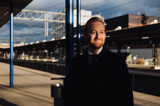 Manlig fastighetsjurist som står på solig pendeltågsperrong