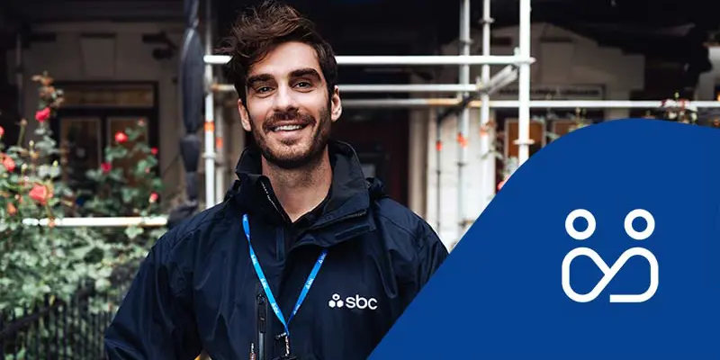 SBCs byggprojektledare Patrik står framför en fastighet med byggnadsställning och rosenrabatt. Projektledningsikon.