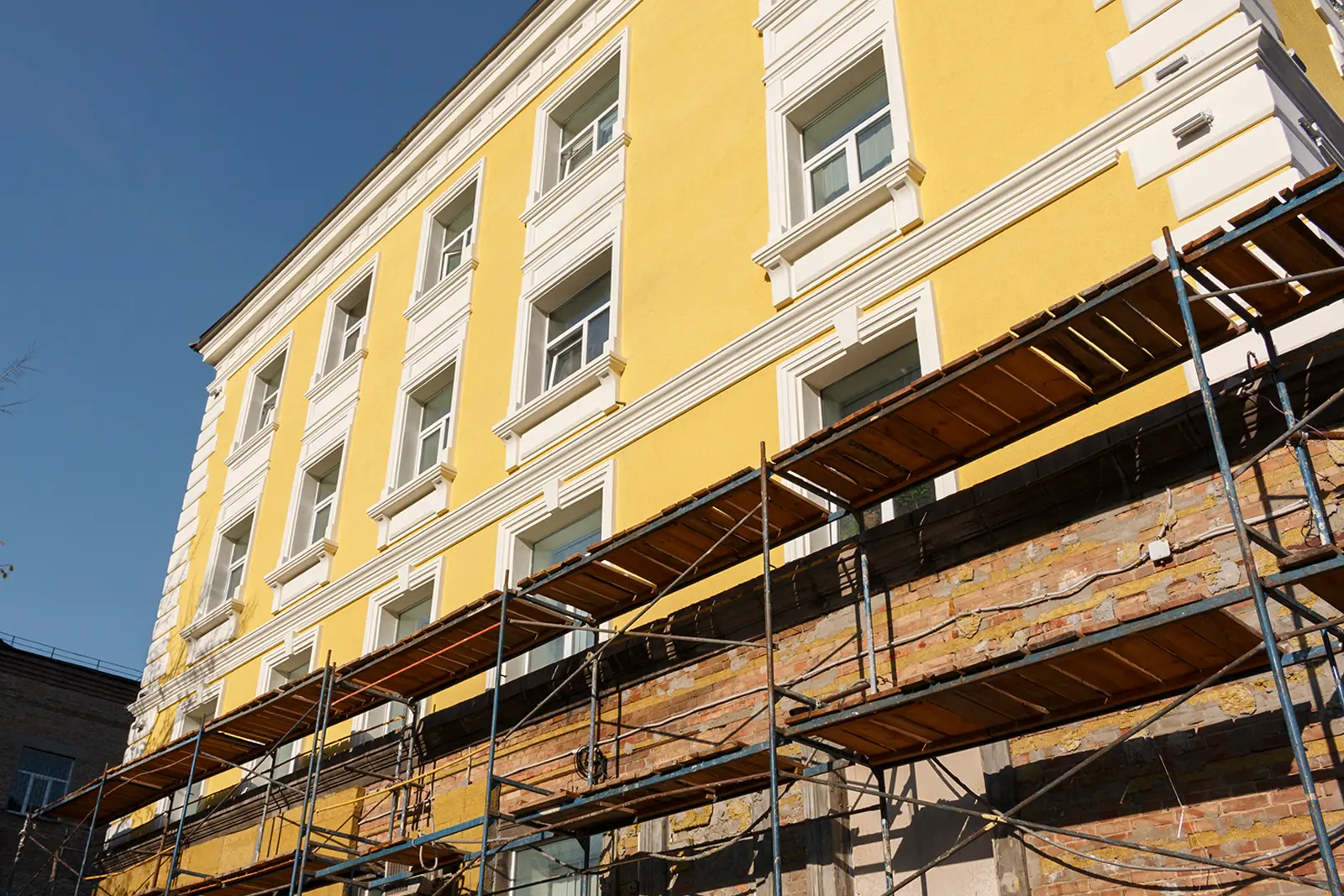 Pågående fasadrenovering av en gul vacker fasad på ett flerfamiljshus.