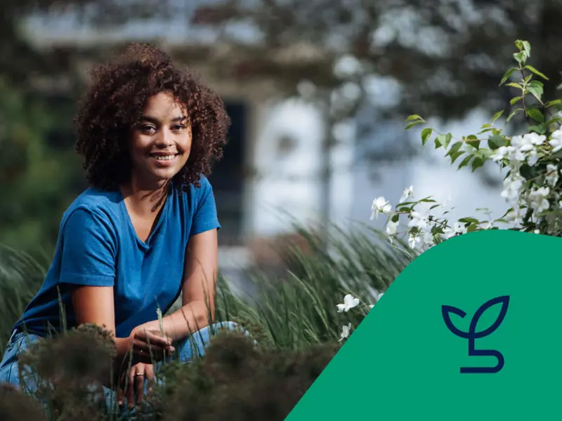 Kvinna sitter på huk i gräset med en fastighet i bakgrunden. Ikon för energi och miljö.