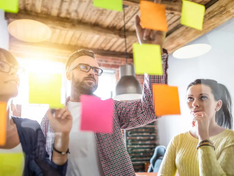Tre människor sätter upp post it-lappar på glasvägg