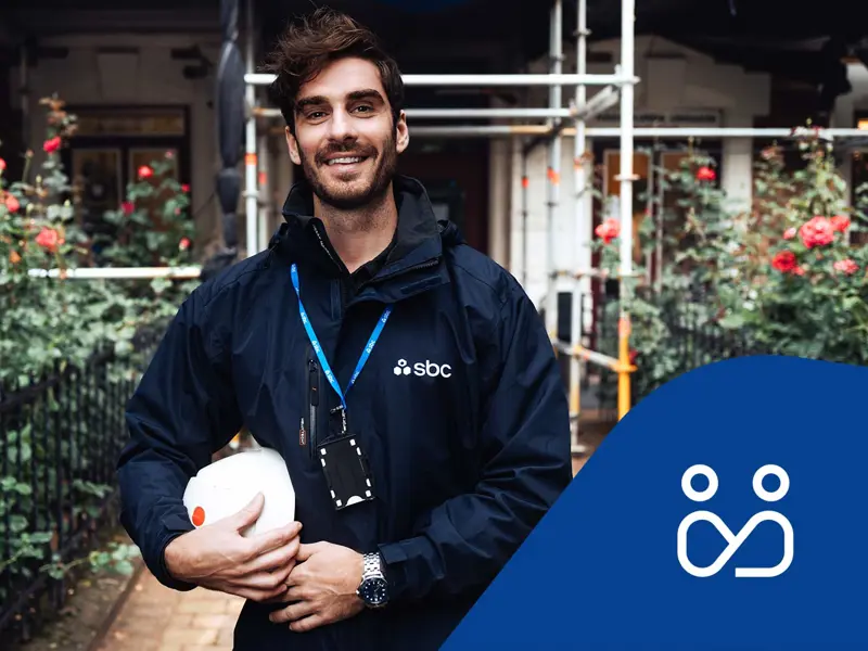 SBCs byggprojektledare Patrik står framför en fastighet med byggnadsställning och rosenrabatt. Projektledningsikon.