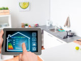 En iPad i förgrunden med smart digitalt system för fastighetens drift och energiförbrukning. Ett kök i bakgrunden.