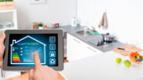 En iPad i förgrunden med smart digitalt system för fastighetens drift och energiförbrukning. Ett kök i bakgrunden.