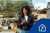 Glad kvinna står på ett torg och tittar i sin mobiltelefon. Ikon för framtidens fastighetsförvaltning.