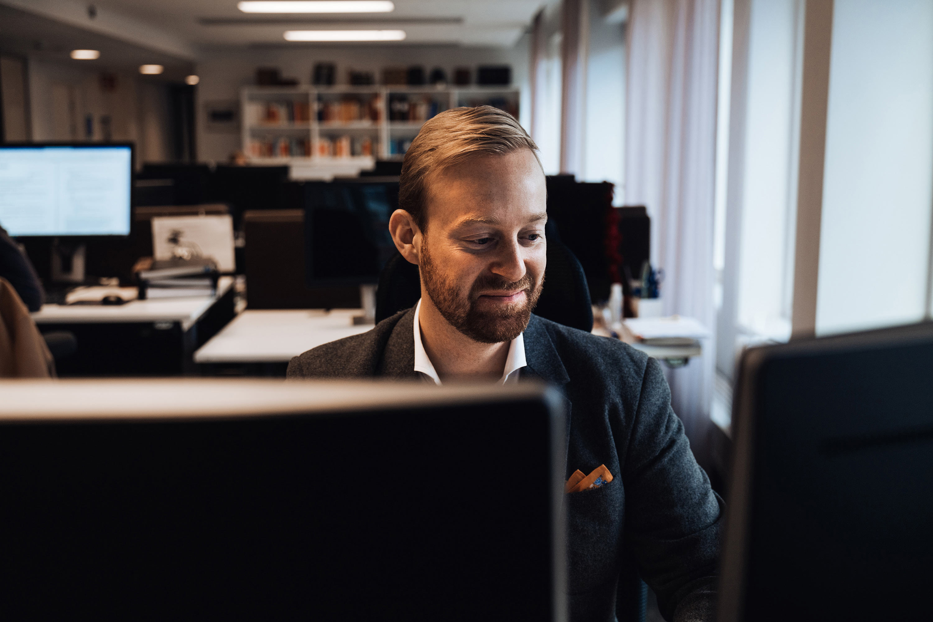 Småleende jurist sitter vid skrivbord med två datorskärmar 