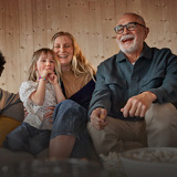 Barn, mamma och farfar tittar på tv tillsammans