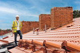 Manlig projektledare iklädd bygghjälm står på taket i en bostadsrättsförening 