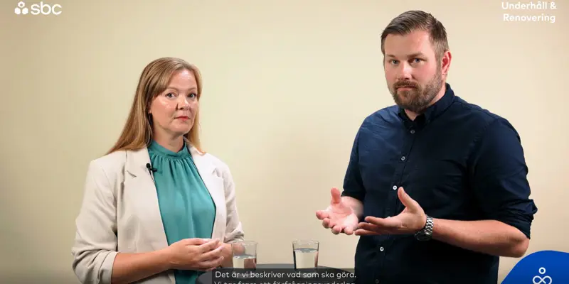 En man och en kvinna står i en studio och samtalar om hur en projektledare avlastar styrelsen i en brf.