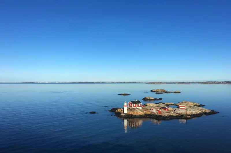 Liten skärgårdsö bebyggd med små röda trähus med vita knutar samt en fyr
