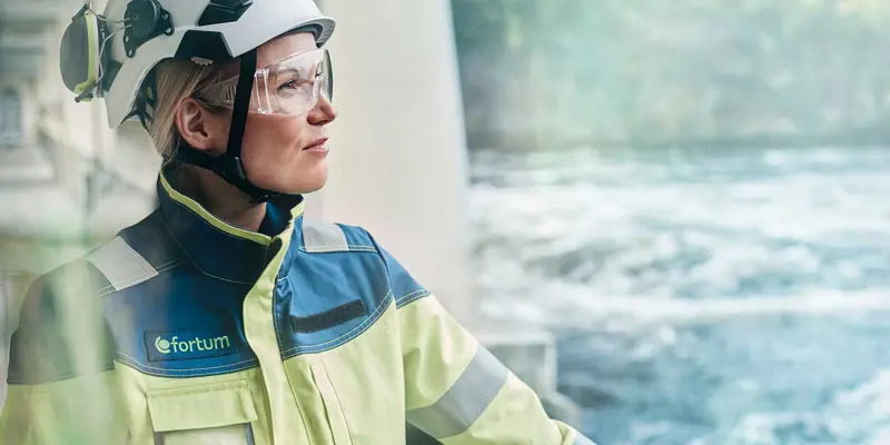 Kvinna med arbetskläder och skyddshjälm blickar ut över vattenfors