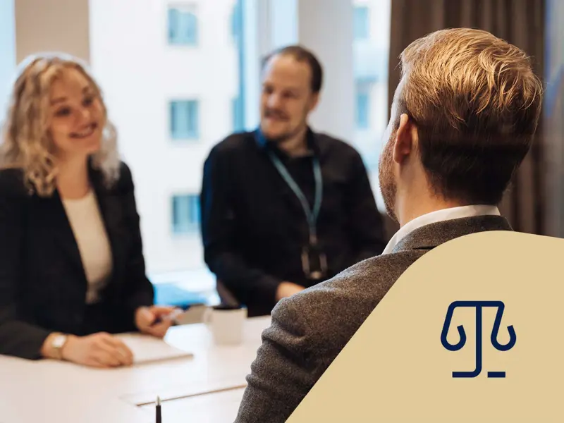 Tre jurister sitter vid ett bord och pratar och ler med ett anteckningsblock. Juridikikon.