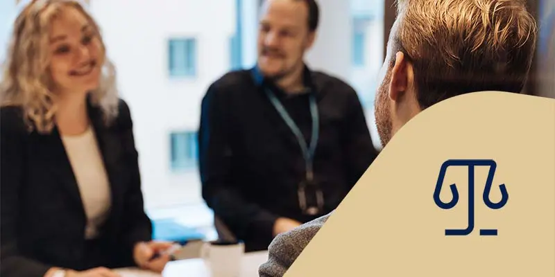 Tre jurister sitter vid ett bord och pratar och ler med ett anteckningsblock. Juridikikon.