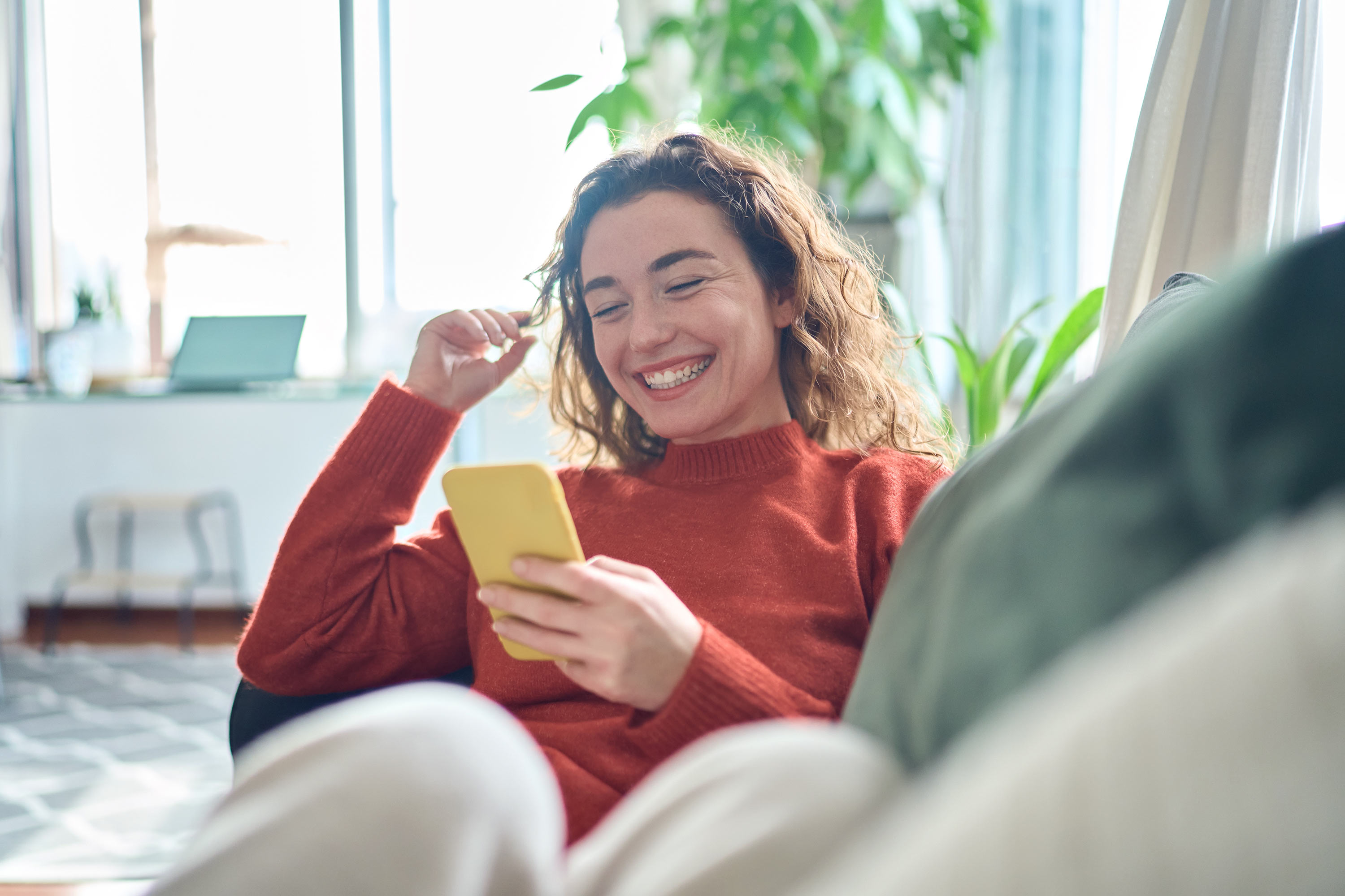 Leende kvinna sitter i soffan med sin mobiltelefon.