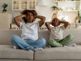 Mamma och son sitter i soffa och håller för öronen, störs av oljud från granne