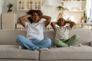 Mamma och son sitter i soffa och håller för öronen, störs av oljud från granne
