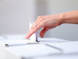 Hand släpper ner röstkort i en låda