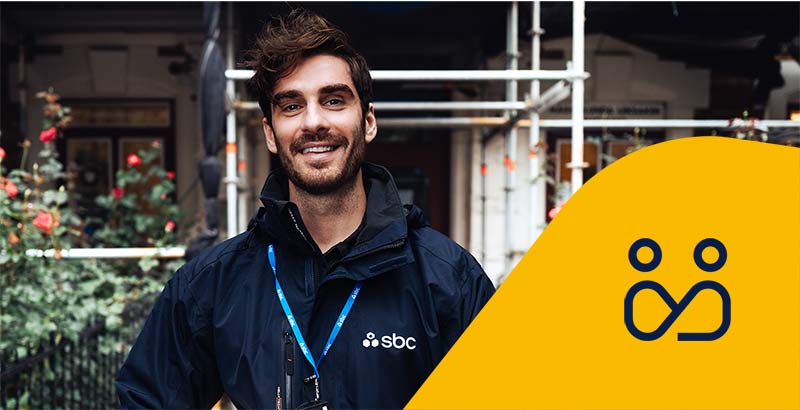 SBCs byggprojektledare Patrik står framför en fastighet med byggnadsställning och rosenrabatt. Projektledningsikon.