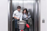 Mamma och pappa med bebis i barnvagn åker hiss tillsammans