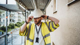 Manlig projektledare går i byggnadsställning och rättar till sin bygghjälm