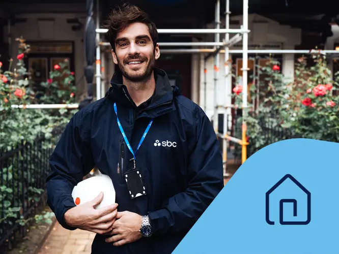 Projektledare Patrik står framför en fastighet med byggnadsställning och rosenrabatt. Fastighetsikon.