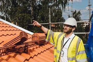 Manlig projektledare iklädd bygghjälm står på taket i en bostadsrättsförening och pekar